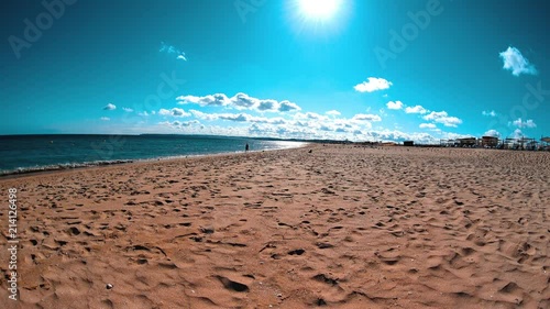 Sunny day at the beach, man walking by coastline, calm waves splashing, nice day at vacation