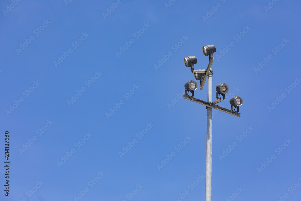 Sports stadium floodlight tower with reflectors with blue sky.