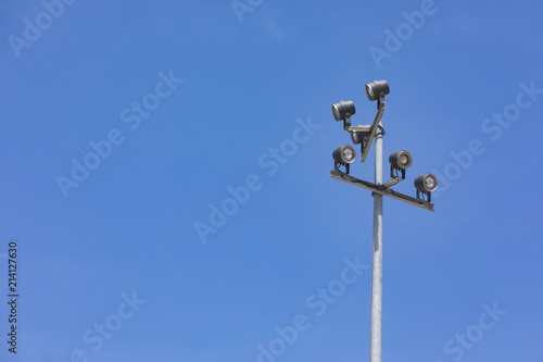 Sports stadium floodlight tower with reflectors with blue sky.