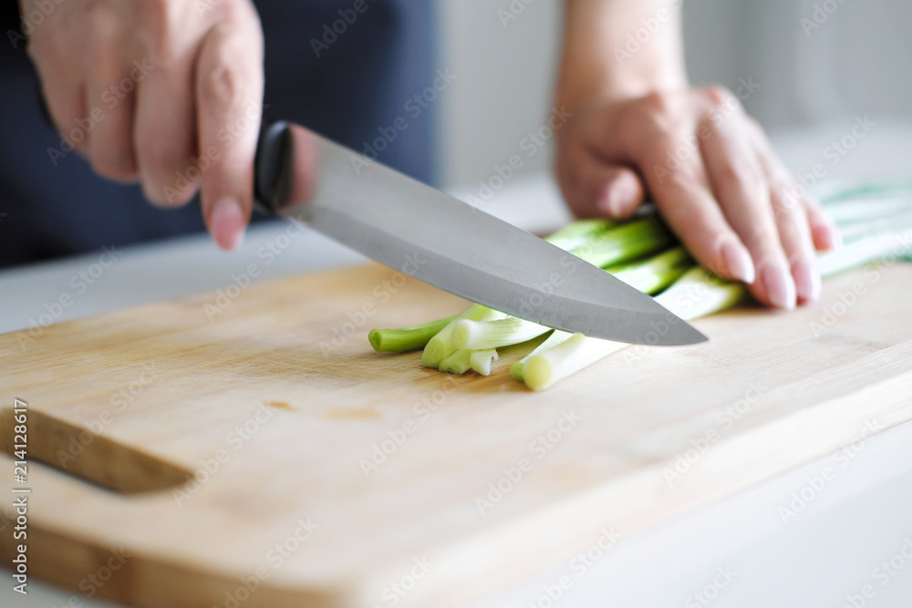Female hands with a knife, slicing vegetables on a wooden board on a white background. Female hands with a knife, slicing vegetables on a wooden board on a white background.