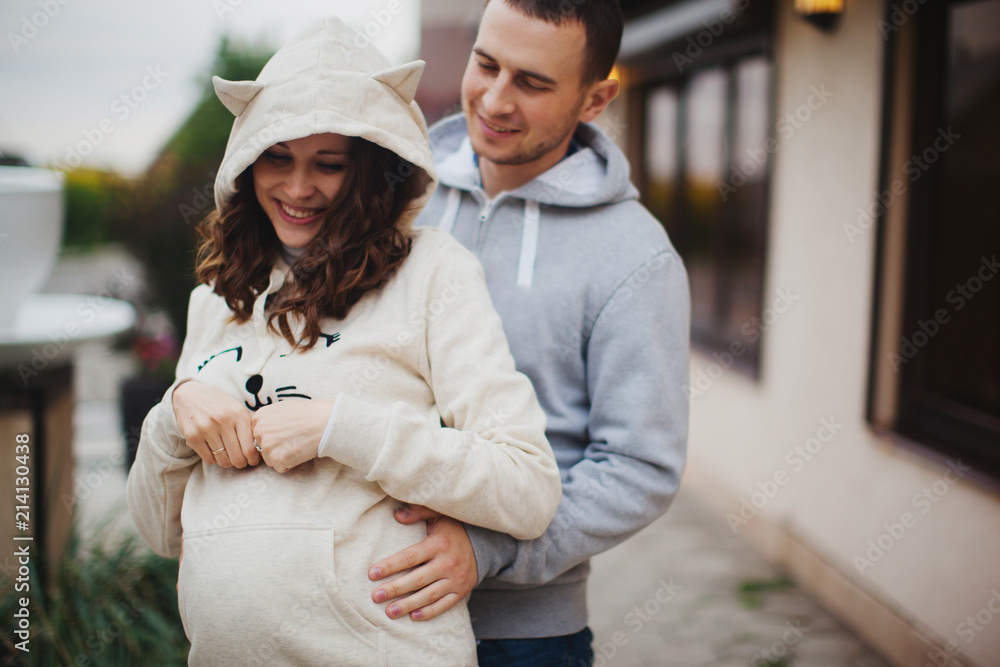 Pregnant woman and her husband wearing hoody. Happy young couple hugging outdoors in the fall