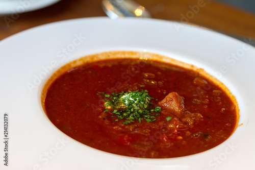 A plate full of warm delicious goulash soup, a spicy stew from Hungary with a vibrant red color due to paprika