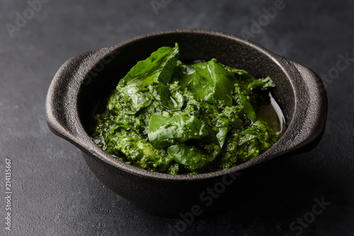 Basil pesto sauce with parmesan cheese, nuts, olive oil and garlic in black cast iron mortar, close up view
