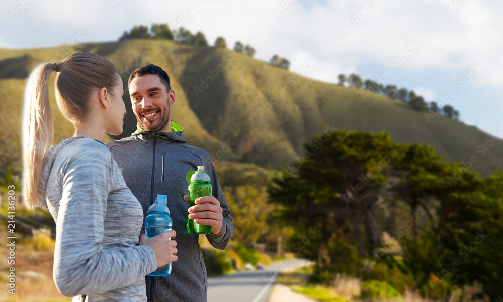 fitness, sport and people concept - smiling couple with bottles of water over big sur hills background in california