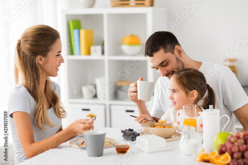 family, eating and people concept - happy mother, father and daughter having breakfast at home
