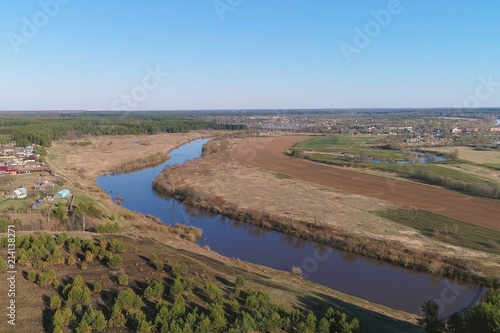 Flight above green fields, forest, river and village early spring, aerial panoramic view photo.