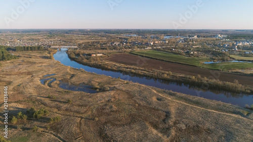 Flight above green fields, forest, river and village early spring, aerial panoramic view photo.