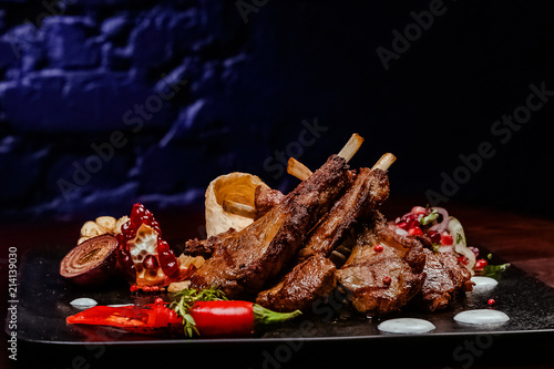 rack of lamb on a black plate decorated with pepper, pomegranate, onion and garlic