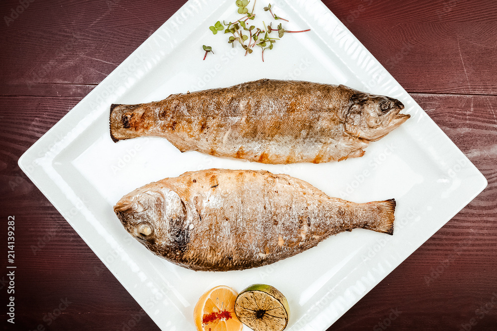 Fried fish on a wooden background. With lemons and spices.