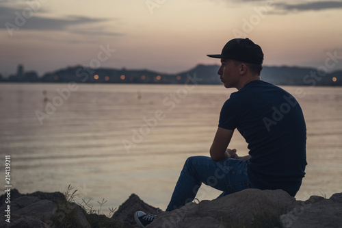 Pensive teen with black cap sitting on the rocks and looking to the sea