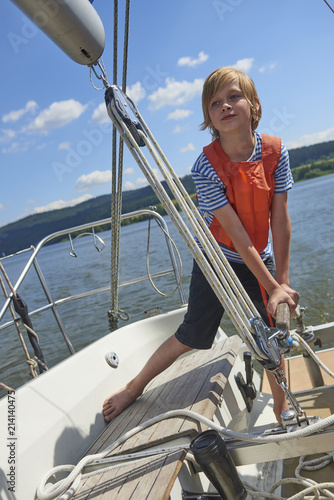  Child boy holding a yacht rudder. Cute boy captain on board of sailing yacht on summer cruise. Travel adventure, yachting with child on family vacation.