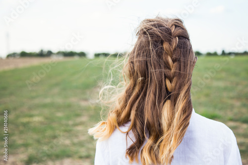 Portrait of young blonde from behind with carelessly braided pigtail and flying hair in wind in field. © alexaphotoua