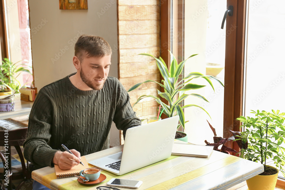 Young freelancer with laptop and notebook working in cafe Young freelancer with laptop and notebook working in cafe