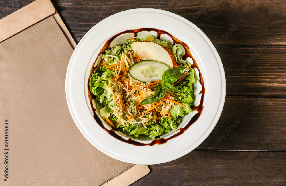 Plate with delicious fresh salad and menu on table, top view Plate with delicious fresh salad and menu on table, top view