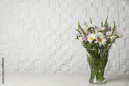 Vase with wild flowers on table near white brick wall