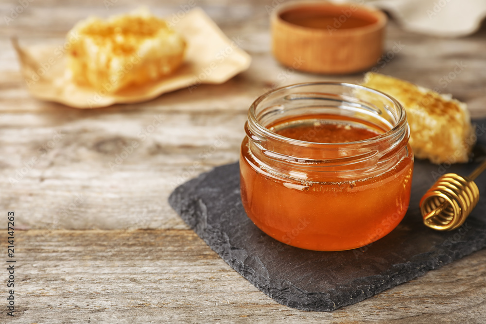 Glass jar with sweet honey and dipper on wooden table, closeup Glass jar with sweet honey and dipper on wooden table, closeup