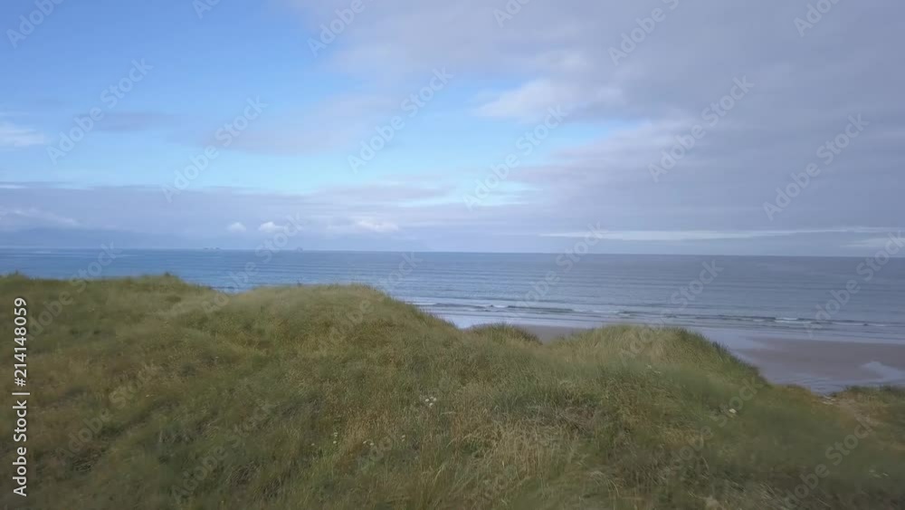 Camera flies over green, grassy sand dunes revealing the vast Atlantic ocean before it. Shot on Banna beach in Kerry, Ireland Camera flies over green, grassy sand dunes revealing the vast Atlantic ocean before it. Shot on Banna beach in Kerry, Ireland