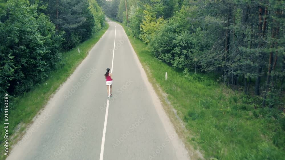 Aerial view of a forest road and a slim young woman running through it Aerial view of a forest road and a slim young woman running through it