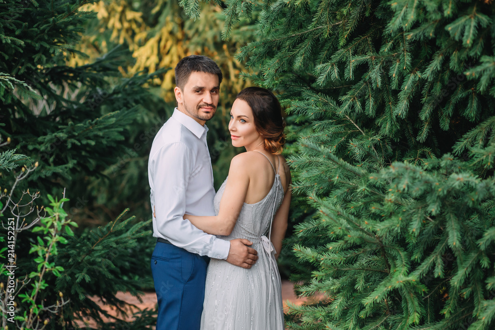 A loving couple is walking in a blooming garden. Red-haired girl in a modest, gray dress in rustic style. Stylish and discreet wedding day. A neat, collected hairdo in an airy beam. Art photo A loving couple is walking in a blooming garden. Red-haired girl in a modest, gray dress in rustic style. Stylish and discreet wedding day. A neat, collected hairdo in an airy beam. Art photo