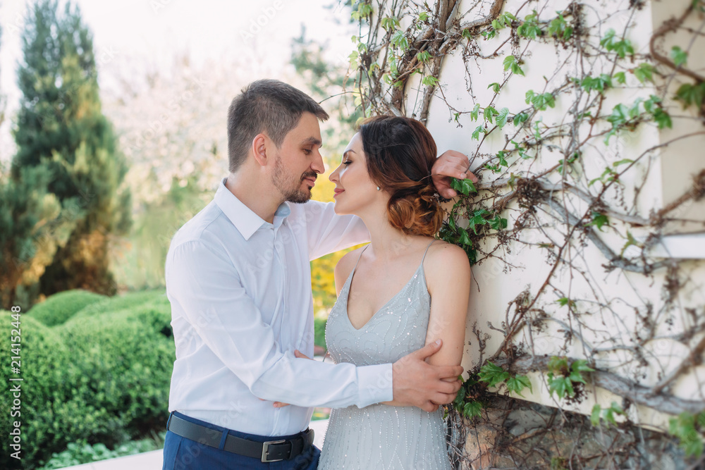 A loving couple hugs in a blooming garden. Red-haired girl in a modest, gray dress in rustic style. Stylish and discreet wedding day. A neat, collected hairdo in an airy beam. Art photo A loving couple hugs in a blooming garden. Red-haired girl in a modest, gray dress in rustic style. Stylish and discreet wedding day. A neat, collected hairdo in an airy beam. Art photo
