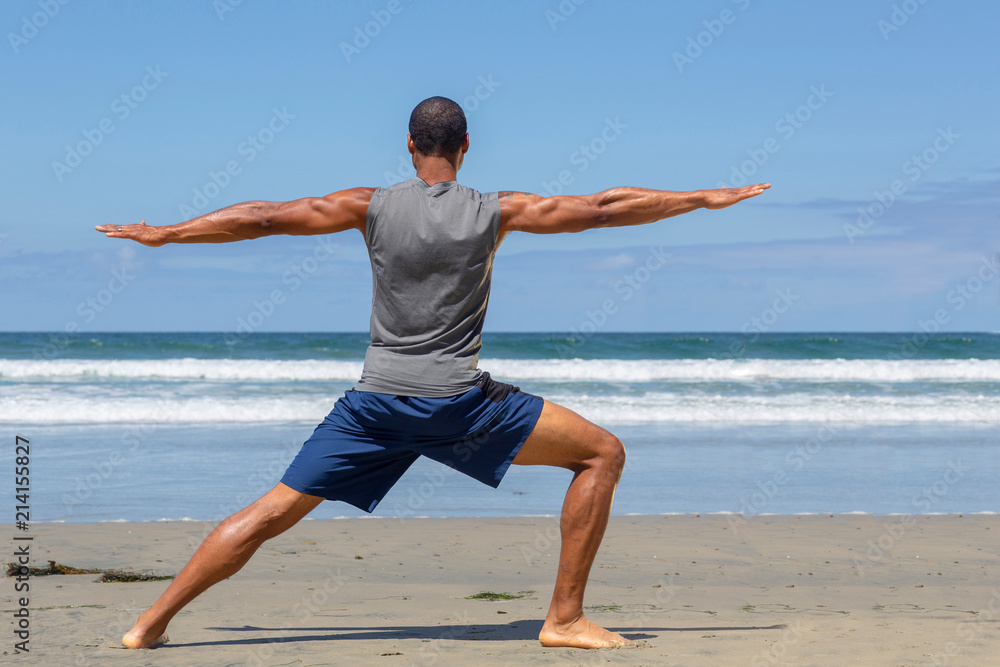 Athletic man at the beach in Warrior ll yoga pose Athletic man at the beach in Warrior ll yoga pose