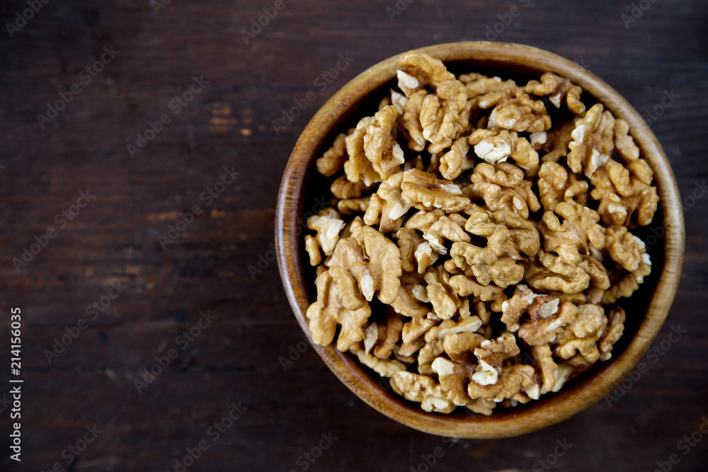 A wooden bowl of walnuts on a dark wooden background top view A wooden bowl of walnuts on a dark wooden background top view