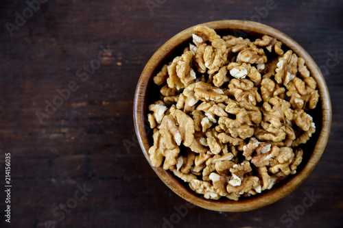 A wooden bowl of walnuts on a dark wooden background top view