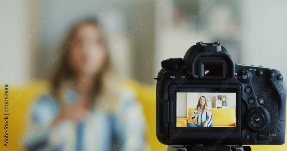 Close up of the camera screen on record with cheerful young woman blogger sitting on the yellow couch in the modern room and having online webinar training. Indoor. Close up of the camera screen on record with cheerful young woman blogger sitting on the yellow couch in the modern room and having online webinar training. Indoor.