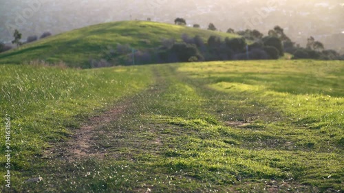 4K walking trail down grassy green hill with city in background