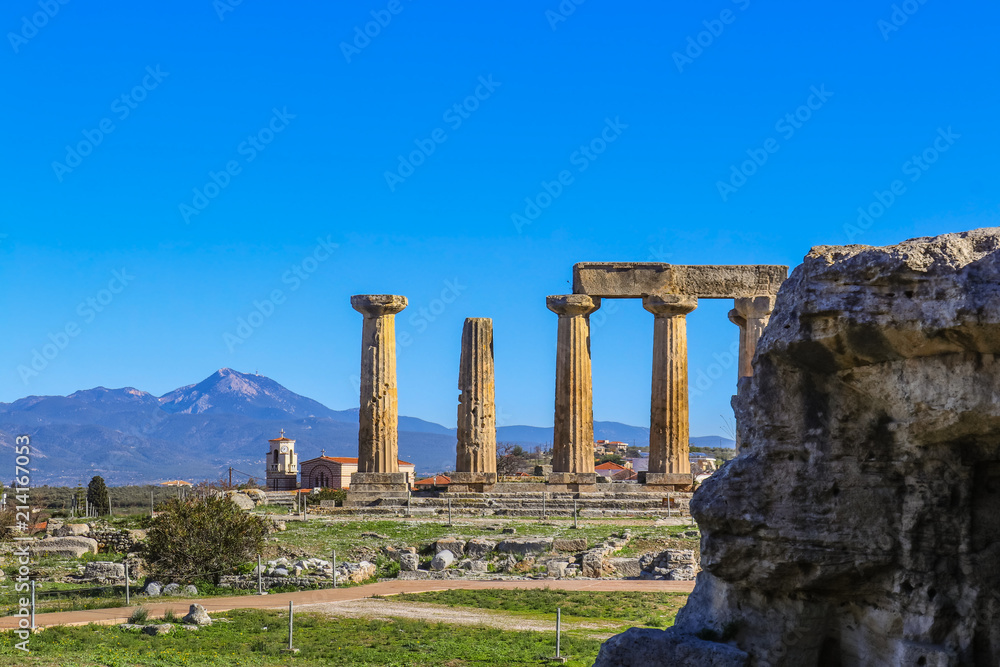 Pillars from Temple of Apollo in Ancient Corinth Greece and background of local picturesque church and mountians on mainland across the Strait of Corinth selective focus