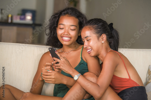 young beautiful and happy Asian girlfriends couple or sisters enjoying internet social media having fun together with mobile phone at home sofa couch