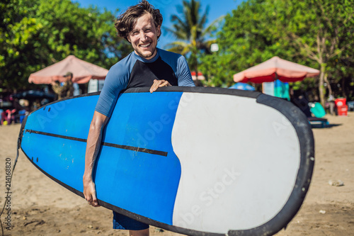 Canvas Print Handsome sporty young surfer posing with his surfboard under his arm in his wets