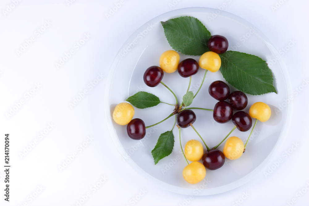 Red and yellow cherries on a white plate, fresh multicolored cherries with green leaves, yellow and red berries in the style of minimalism, vegetarian food, blank for the designer Red and yellow cherries on a white plate, fresh multicolored cherries with green leaves, yellow and red berries in the style of minimalism, vegetarian food, blank for the designer