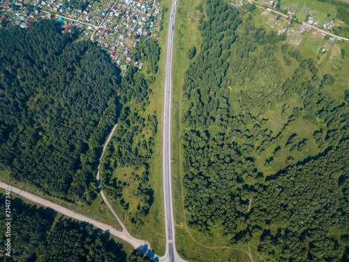 Top view of road, a green forest and a large field in a warm sunny summer day. Helicopter drone shot.