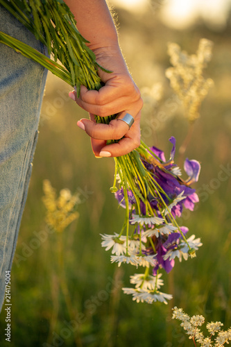 A bouquet of wildflowers in a woman's hand. Sunset.