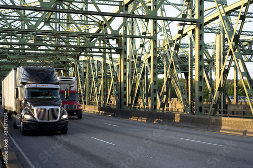 Big rigs semi trucks of different class and size driving on the metal Columbia bridge