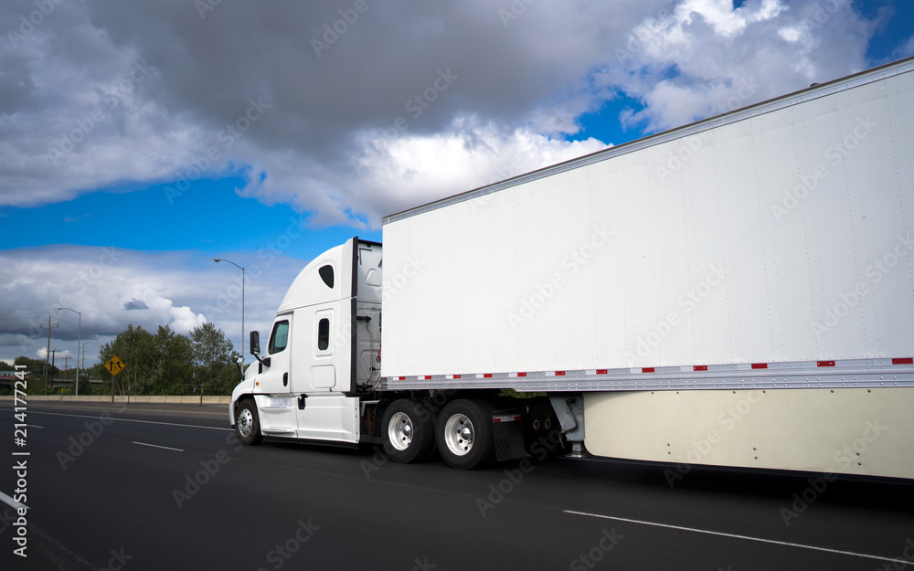 Long haul big rig semi truck transporting commercial cargo in dry van semi trailer on the wide highway with clouds sky Long haul big rig semi truck transporting commercial cargo in dry van semi trailer on the wide highway with clouds sky