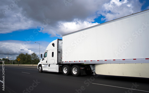 Long haul big rig semi truck transporting commercial cargo in dry van semi trailer on the wide highway with clouds sky