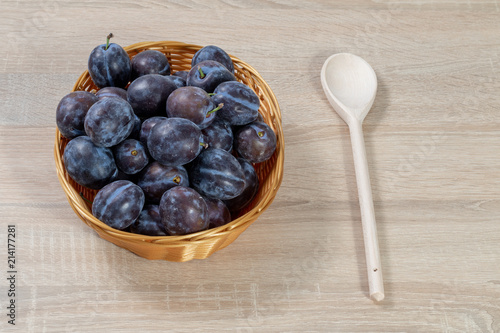Wooden spoon beside a basket full of ripe plums