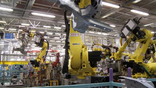 The group of robots in an automatic mode perform joint work on assembling and welding of the body of a modern car