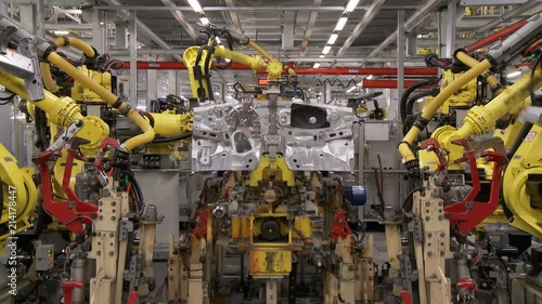 The group of robots in an automatic mode perform joint work on assembling and welding of the body of a modern car