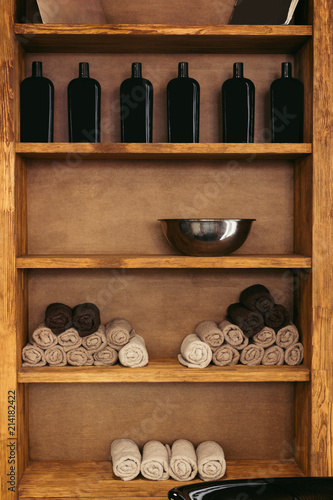 empty metal bowl, rolled towels and glass bottles on wooden shelves in barbershop