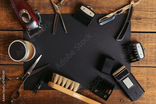 Top view of various professional barber tools on black card on wooden surface