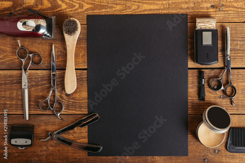 top view of professional barber tools and blank black card on wooden table