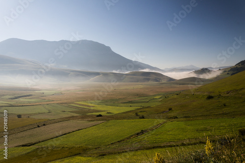 View of Castelluccio di Norcia (Umbria) at dawn, with mist, big meadows and totally empty blue sky