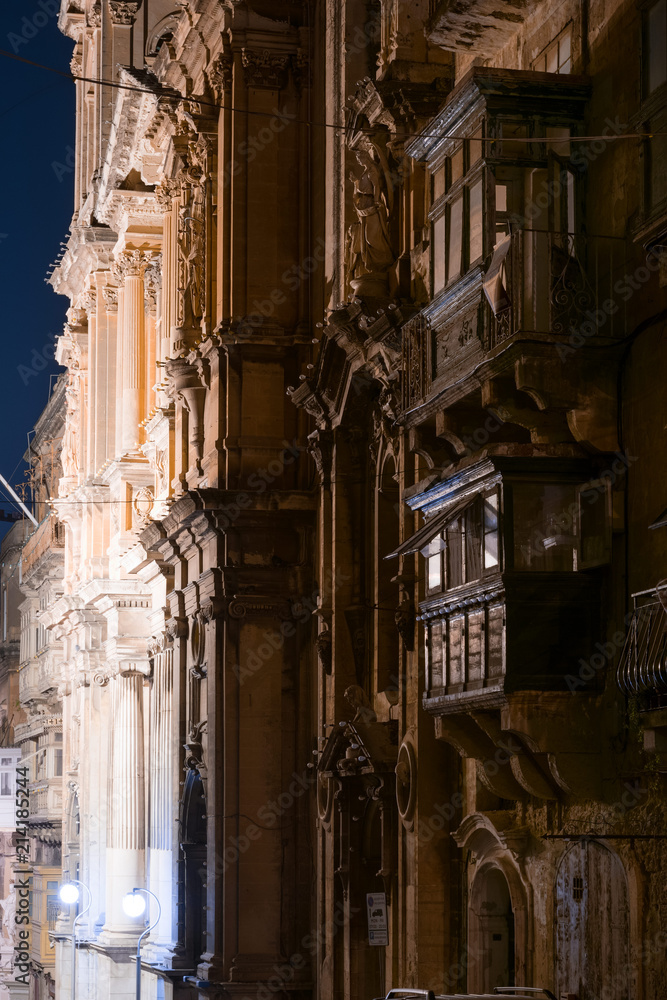 Old medieval street in Valletta, Malta, at night, with hanging balconies.