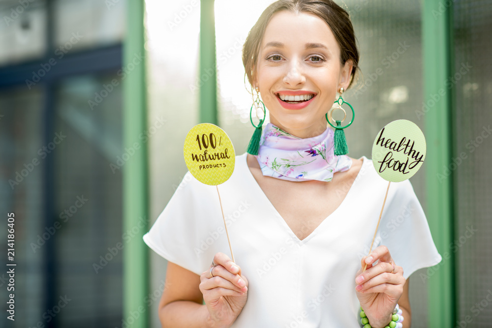 Beautiful woman holding green plates with healthy eating slogans outdoors on the green background Beautiful woman holding green plates with healthy eating slogans outdoors on the green background