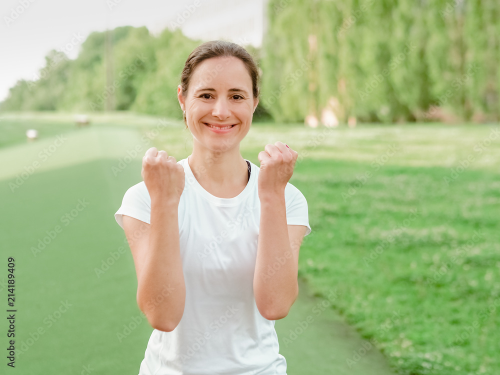 happy smiling femal Fitness Coach in white sportswear making fists outside in the park happy smiling femal Fitness Coach in white sportswear making fists outside in the park