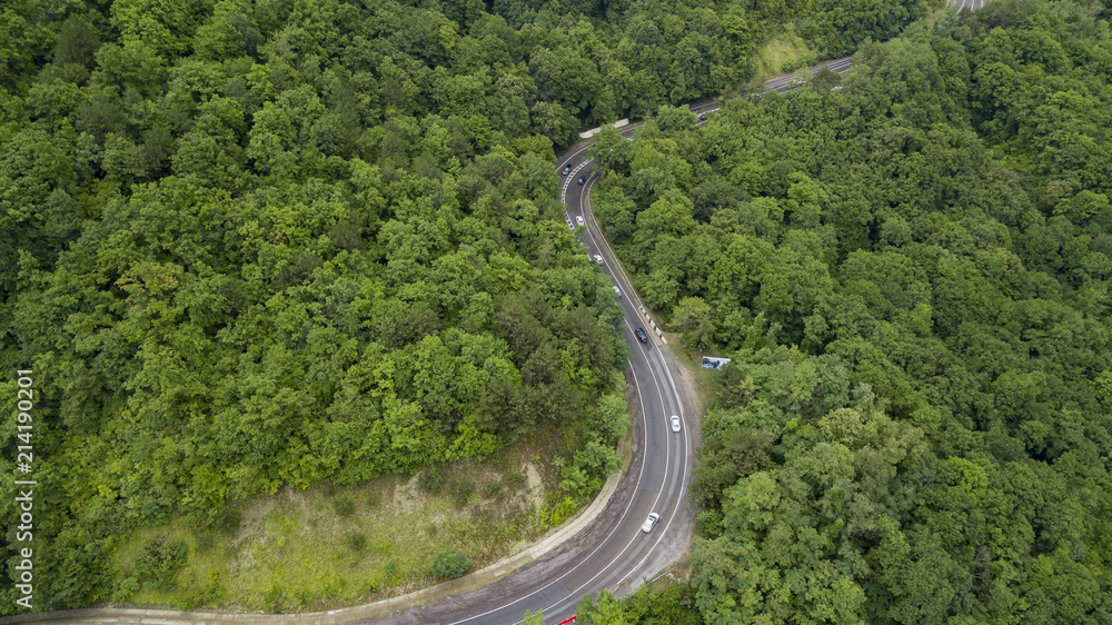 Aerial stock photo of car driving along the winding mountain pass road through the forest in Sochi, Russia. People traveling, road trip on curvy road through beautiful countryside scenery.