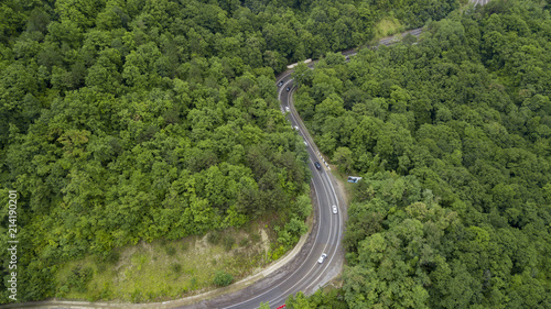 Aerial stock photo of car driving along the winding mountain pass road through the forest in Sochi  Russia. People traveling  road trip on curvy road through beautiful countryside scenery.